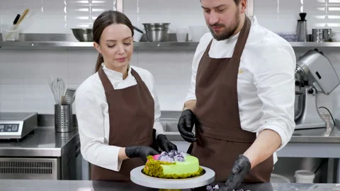 Two pastry chefs, a man and a woman, twist a cake on a stand. Stock Footage 170103404