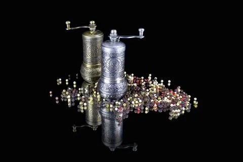 Two patterned silver pepperpots and pepper balls scattered around on black Stock Photos
