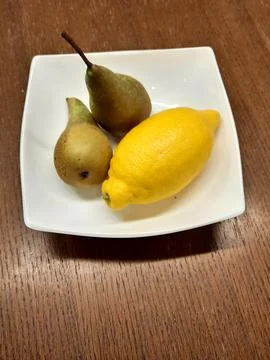 Two pears and lemon in white bowl on wooden table Stock Photos