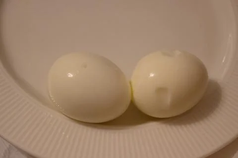 Two peeled boiled eggs on a white plate Stock Photos