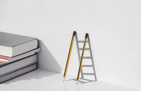 Two pencils and shadow in form of ladder with stack of textbooks on white t.. Stockfoto's