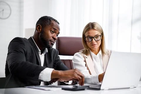 Two people analyze documents on a laptop while sitting at a table in the office Stock Photos