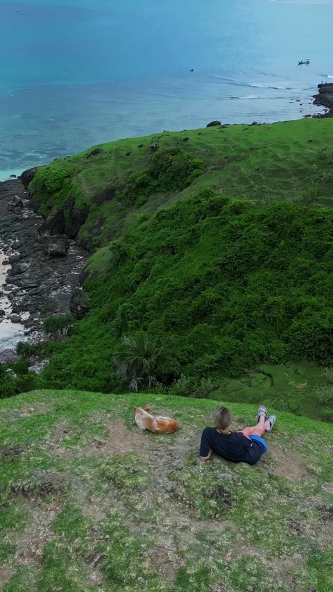 Two people and their pet relaxing at serene coastal overlook Stockbeeldmateriaal 335223262