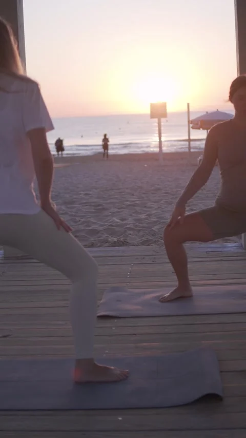 Two people are practicing yoga on mats by the beach during sunrise Stock Footage 317549638
