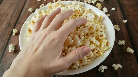 Two people are simultaneously reaching for popcorn in a white bowl top view,  Stock Footage 132781067