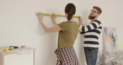 Two people are standing in new apartment near the wall. Woman checks level of Stock Footage 147059840