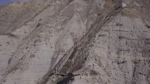 Two people are walking down stairs and seat at a beach near the cliffs 스톡 동영상 86902580
