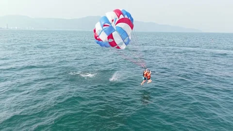 Two people attached to a red, white, and blue parachute, parasailing over the Stock Footage 333375331