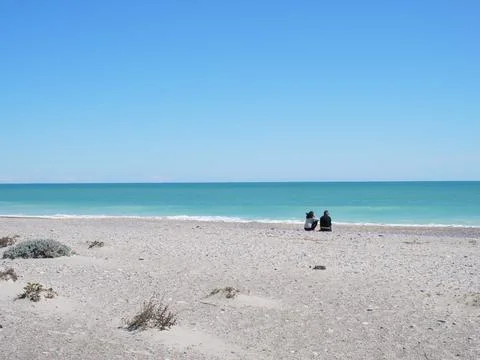 Two people from the back sitting facing the sea on the deserted beach Stock Photos