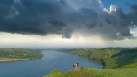 The two people with backpacks standing on the mountain top above scenic river Stock Footage 159841511