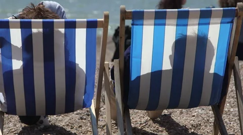 Two people in deck chairs on a shingle beach Stock Footage 41276702