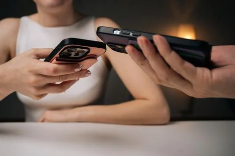 Two people exchanging data using mobile phones sitting at white table at home Stockfoto's