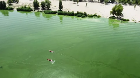 Two people float on a kayak along a sad beach on the green water surface. View Stock Footage 135823404