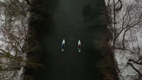 Two people float on a sap board on a calm river by snow banks Video stock 299533900