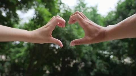 Two people forming a heart shape with their hands against a green background Stock Footage 341948648