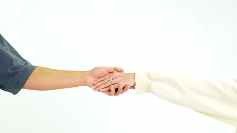 Two people gently hold hands wearing engagement rings against a plain white Видео 326611336