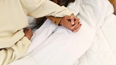 Two people gently hold hands on a white bed, symbolizing emotional support Stock-Footage 326611350
