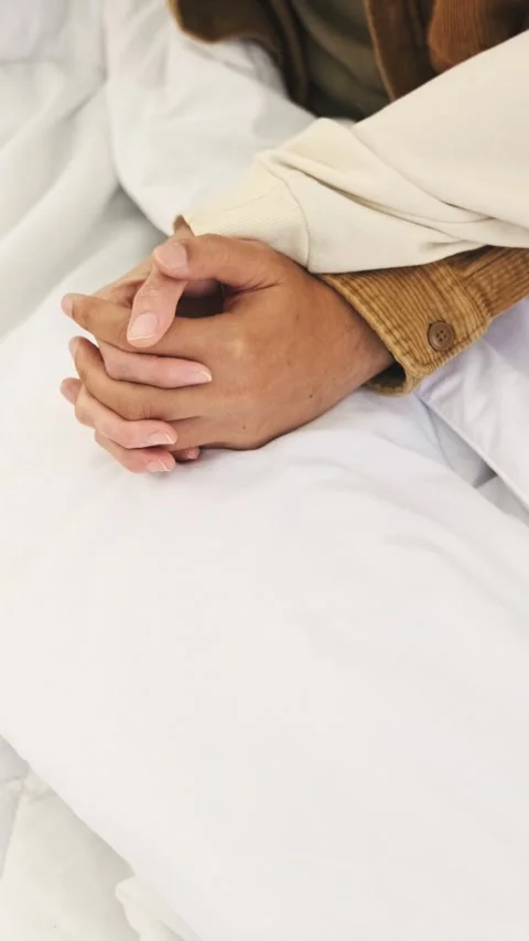 Two people gently hold hands on a white bed, symbolizing emotional support Video stock 327789586