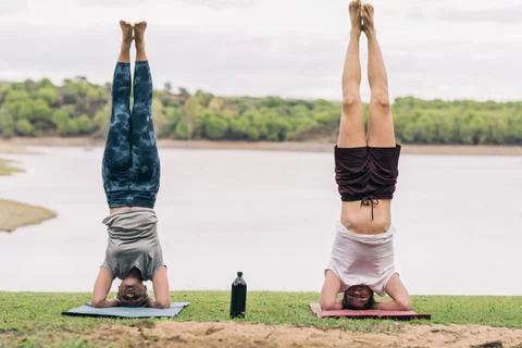 Two people with the head on the floor practising yoga in a park with a lake Stock Photos