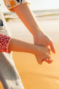 Two people hold hands while walking on beach during sunset with waves in back Stock Photos