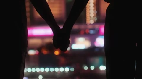 Two people holding hands in front of a vibrant cityscape at night Stock-Footage 329616181