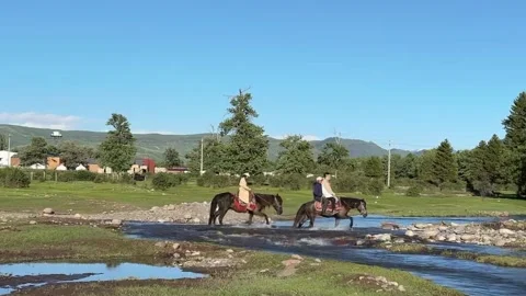 Two people on horseback cross a clear stream in Xinjiang grasslands, China. Vídeos de archivo 337443043