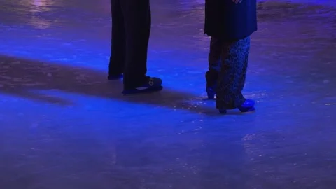 Two people ice skating on a glossy rink under vibrant purple light, capturing a Stock Footage 345665586