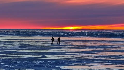 Two people ice skating together on a frozen lake during a colorful winter sunset Stock Footage 346594474