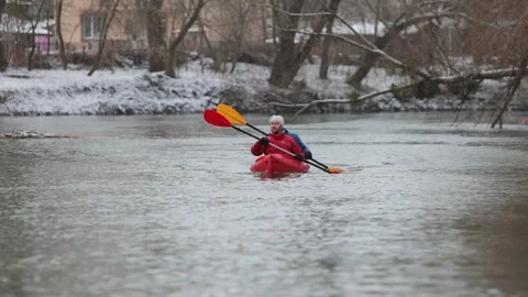 Two people kayaking on a calm river during winter with snowy banks and overcast Video stock 299711146