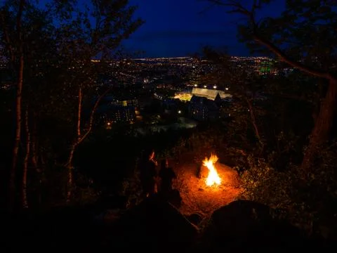 Two people looking at campfire overlooking city in the background at night. Stock-Fotos