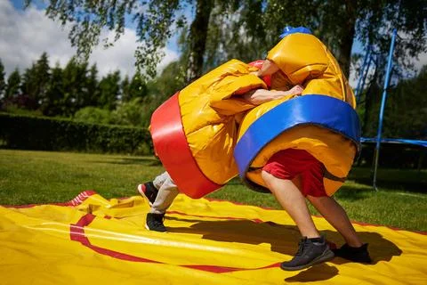 Two people in oversized inflatable sumo suits wrestling on a yellow and red m Stock Photos