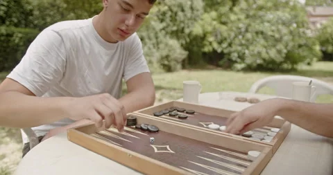 Two people play backgammon at an outdoor table on a bright, sunny day, depicting Stockbeeldmateriaal 284650290