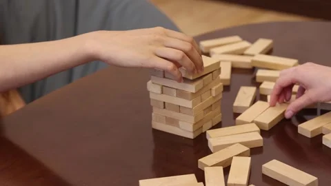 Two people play blocks game, carefully removing wooden blocks from  tower Stock Footage 278888908