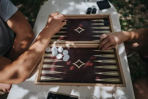 Two people playing backgammon outdoors under dappled sunlight Stock Photos