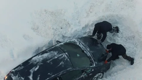 Two people push car stuck in deep snow, struggle during winter, road covered Stock Footage 344864929