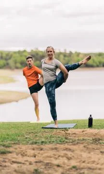 Two people raising leg while doing yoga in a park Stock Photos