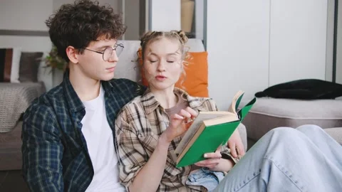 Two people read a book together in a cozy indoor space while sitting close to Stock Footage 346186047