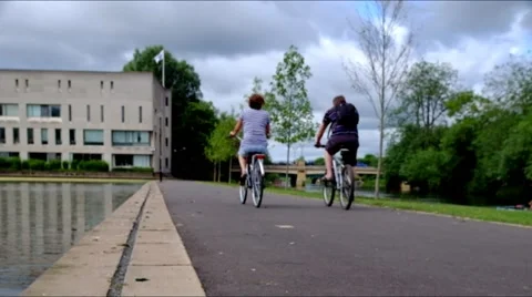 Two people ride bicycles on a path by water Stock Footage 45842749