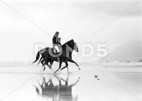 Two People Riding Horses On Beach, Side View, B&w.