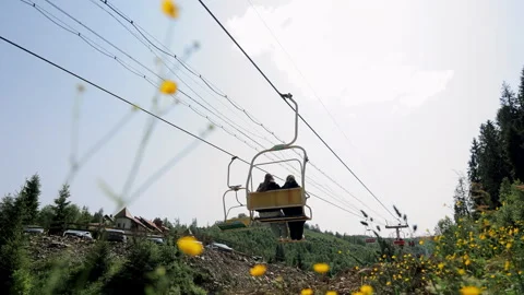 Two people riding open mountain chairlift above scenic countryside with yellow Stock Footage 312740683