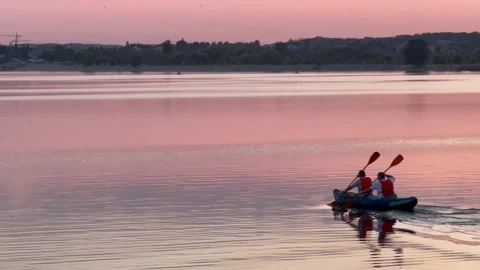 Two People Rowing a Boat Across a Lake at Pink Sunset Stock Footage 346380120