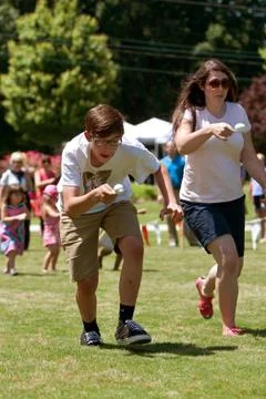 Two people run in egg and spoon race at festival Stock Photos
