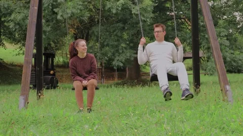 Two people share a joyful moment while swinging in a tranquil park Stock Footage 316608587