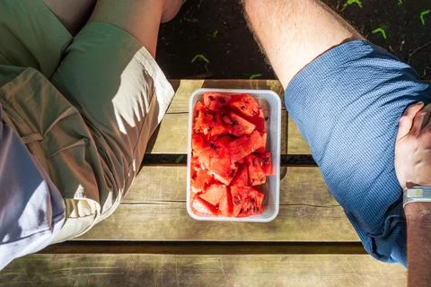Two people share watermelon snack on bench after walking in forest Foto stock