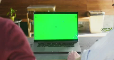 Two people sit at a table in a cafe in front of an laptop with a green screen Stock Footage 166589968
