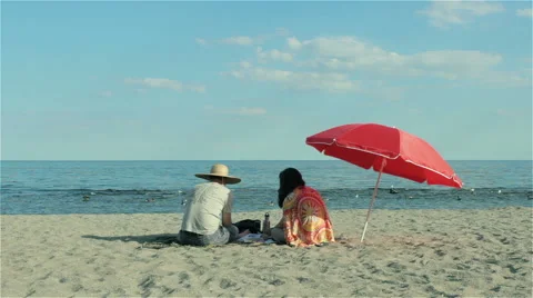 Two people sitting on the beach under red parasol Video stock 52695167