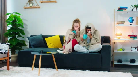Two people sitting on the couch sneezing into tissue, they look pale and sick Video stock 145474444