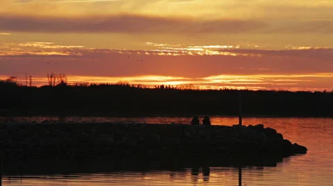 Two people sitting on pier at sunset Stock Footage 37227414