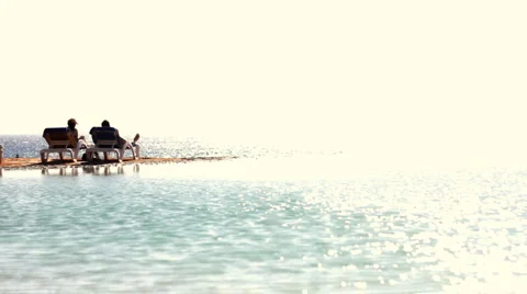 Two people sitting on sunbeds at the beach during sunbathe Stock Footage 1068300