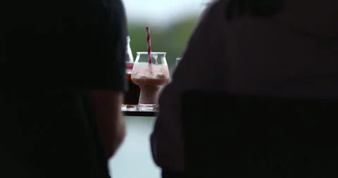 Two people sitting at table with drinks by lakeside 스톡 동영상 332622066